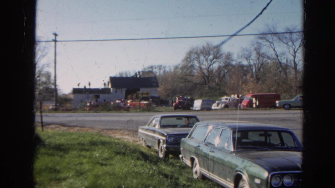 1968 Wauconda roadside view with a green station wagon and dark sedan parked in the foreground near a barnhouse across the road.