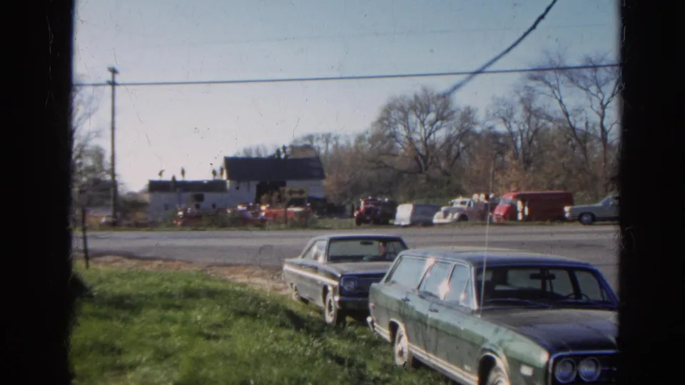 1968 Wauconda roadside view with a green station wagon and dark sedan parked in the foreground near a barnhouse across the road.