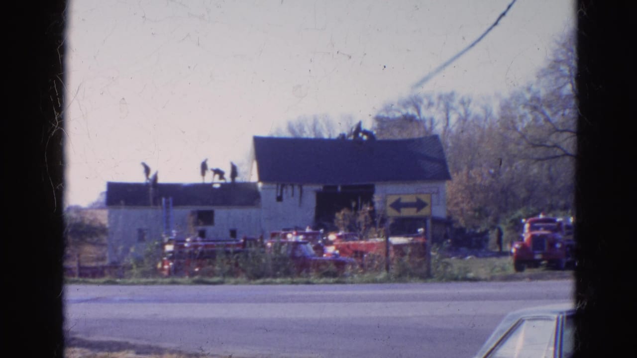 White roadside cabin with people on the roof, red vehicles, and a yellow two-way arrow sign.