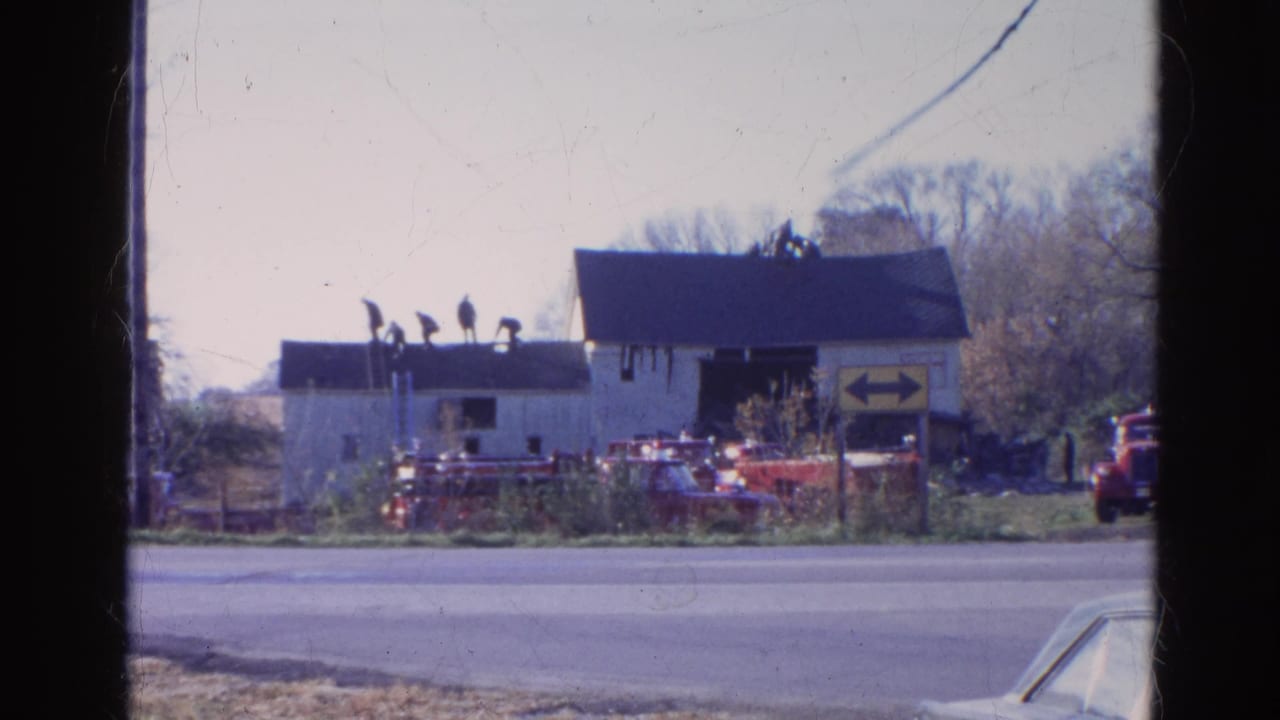 Distant view of men on a roof above a white building with red emergency vehicles nearby.