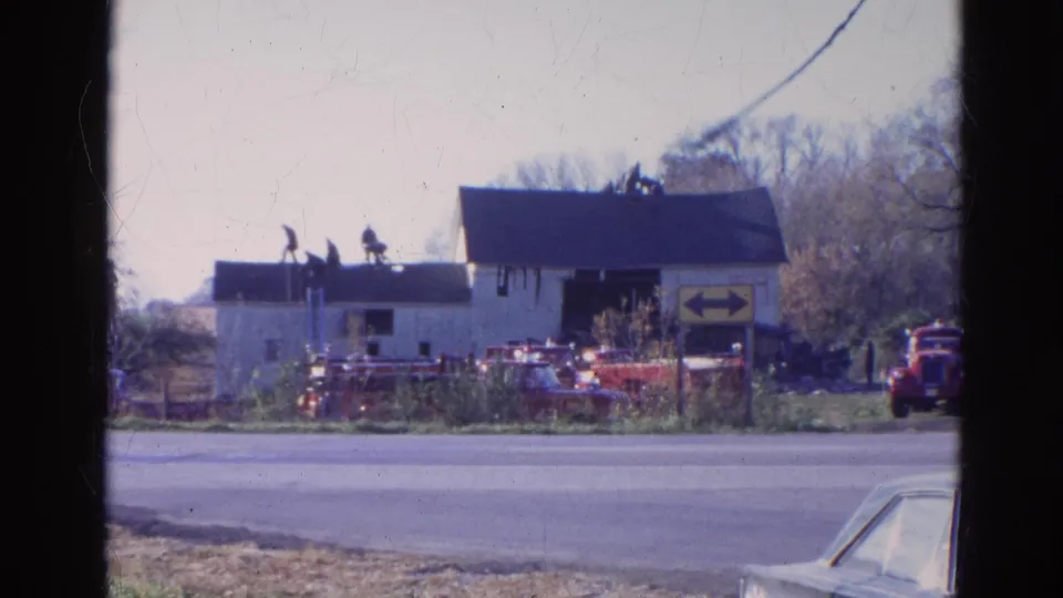 1968 Wauconda, Illinois frame with roof figures, red fire apparatus, a directional sign, and a partial car at the roadside edge.