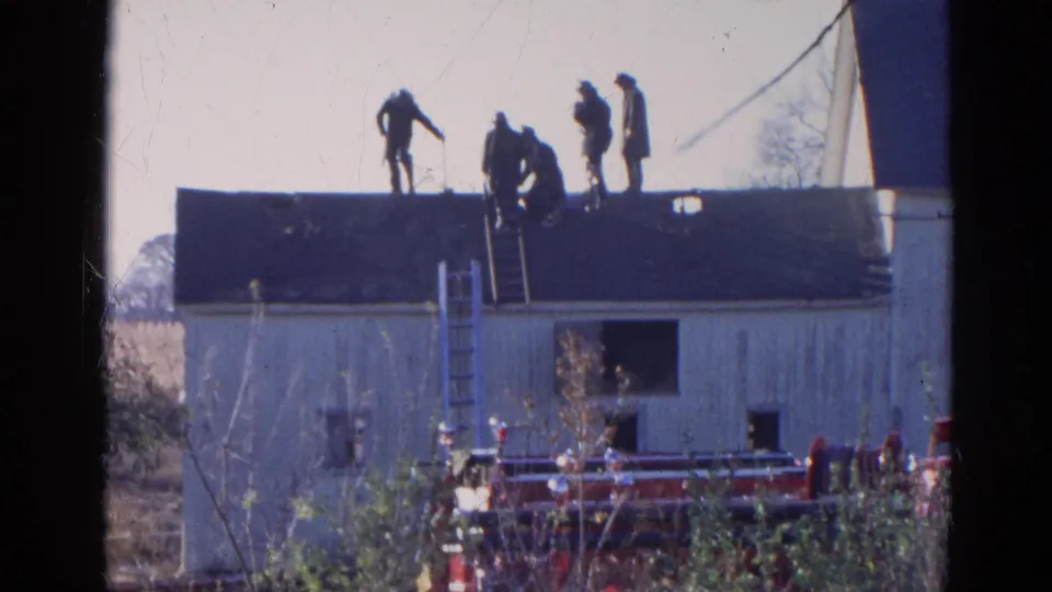 Five men appear on the roof of a white building in 1968 Wauconda, with ladders set against the roof and a fire truck below.