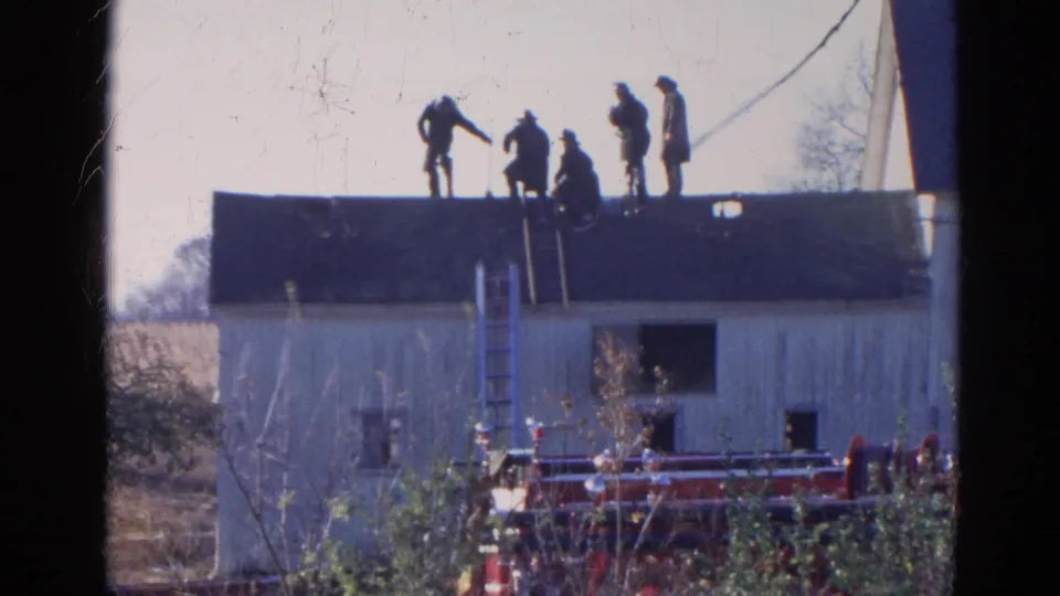 The 1968 Wauconda home movie shows men coordinating roof work on a white building, filmed from a distant outdoor position.