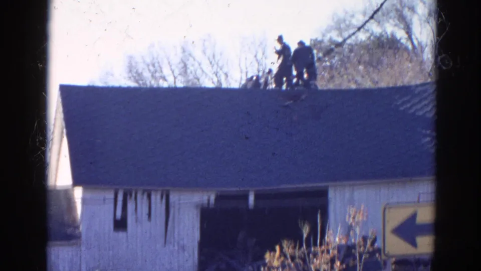 Firefighters remain on the roof of the damaged Wauconda building in this brief 1968 8mm fire response view.