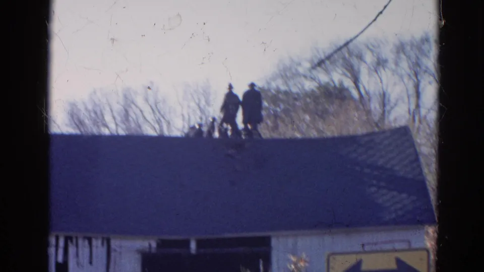 1968 Wauconda, Illinois 8mm still of two silhouetted people on a roof above a barn-like exterior.