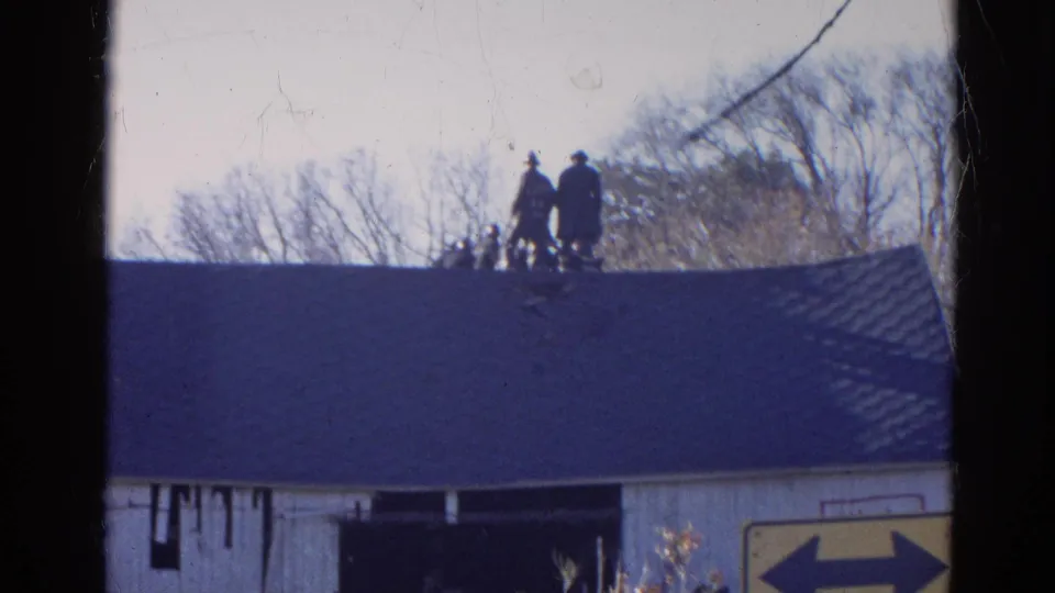1968 Wauconda, Illinois home-movie frame showing people on a roof with a white building and sign below.