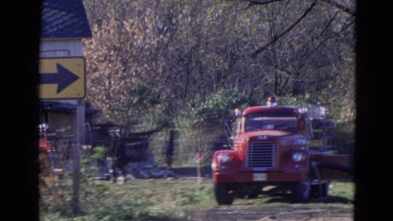 Red fire truck on a grassy drive near woods and a yellow right-arrow sign.