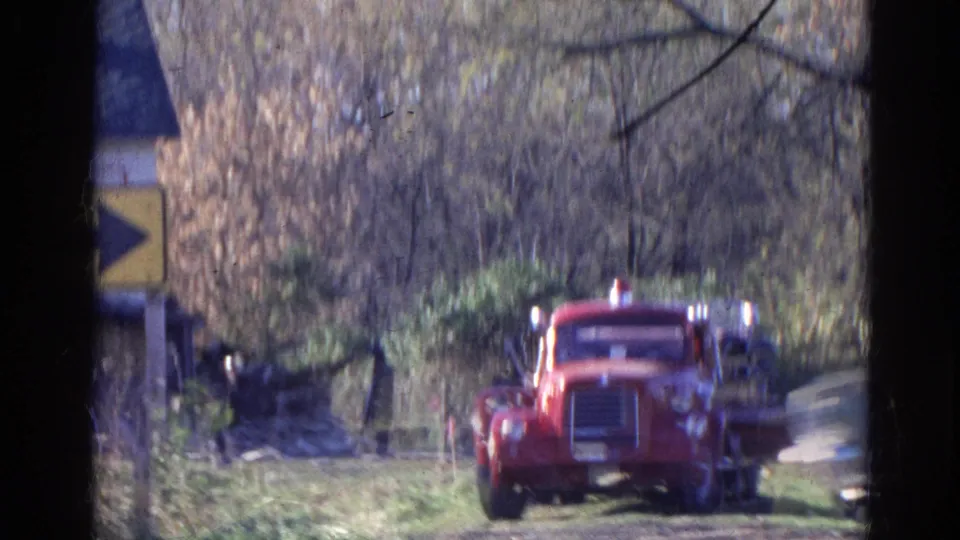 Soft 8mm frame from Wauconda, Illinois, showing the red fire truck, roadside sign edge, and wooded emergency scene.