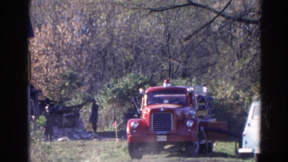 1968 Wauconda, Illinois frame showing a red fire truck in a grassy wooded area with equipment and a pale vehicle edge nearby.