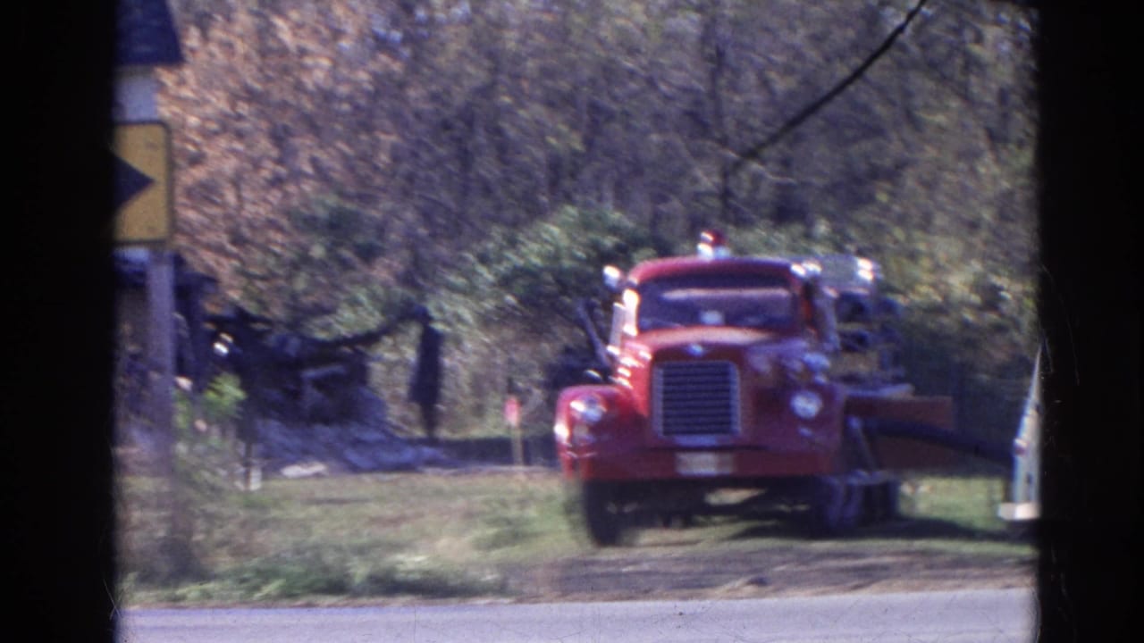Red fire truck facing the camera near a grassy rural area, partly obscured by dark window framing.