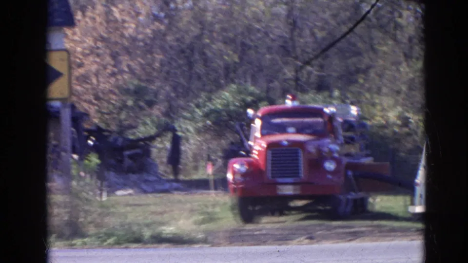 1968 Wauconda, Illinois home-movie frame showing a red fire truck from the front in a wooded rural setting, with dark framing in the foreground.