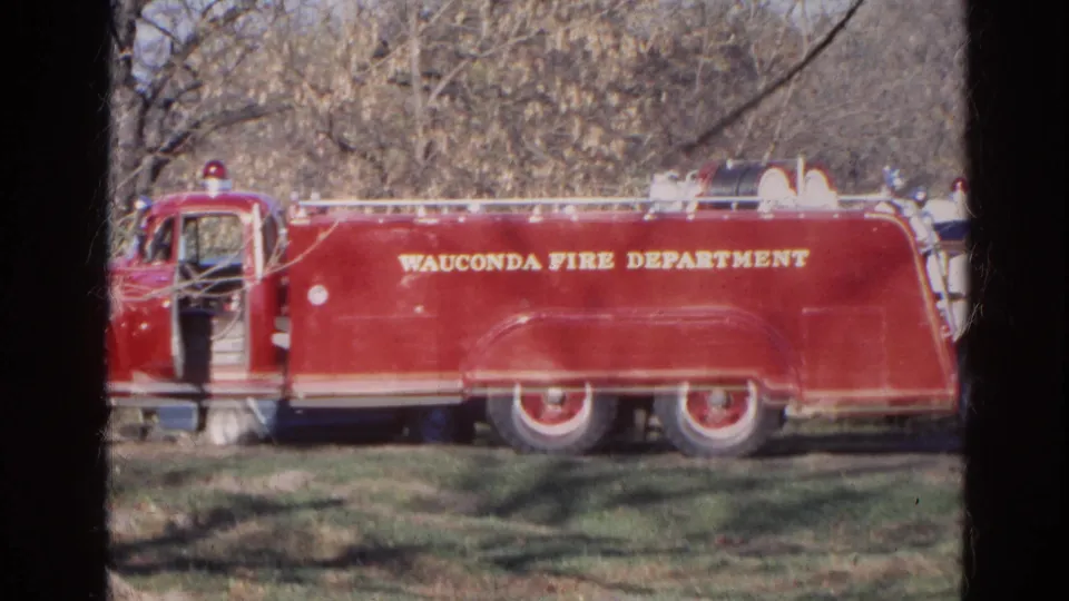1968 Wauconda, Illinois frame showing a red fire department truck broadside, with yellow lettering, open door area, and rural trees in back.