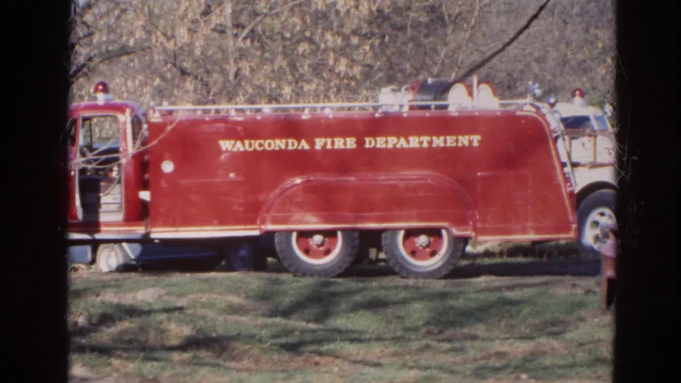 1968 Wauconda, Illinois frame showing the red Wauconda Fire Department truck in side view, with a partial white vehicle and trees nearby.