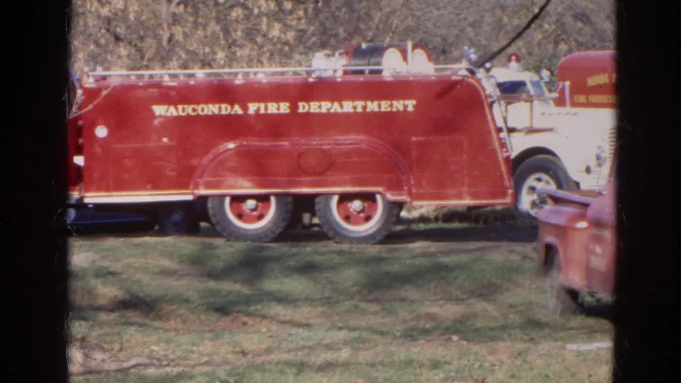 Side view of the Wauconda Fire Department truck in a rural Illinois setting, with bare trees and a partial vehicle nearby.