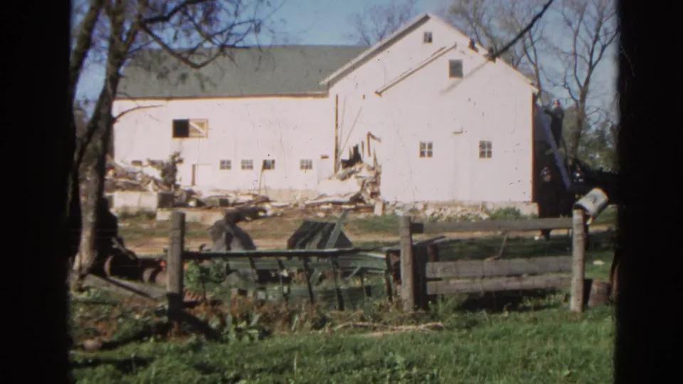 1968 Wauconda, Illinois view of a white barn with visible damage and scattered debris beyond a wooden fence.