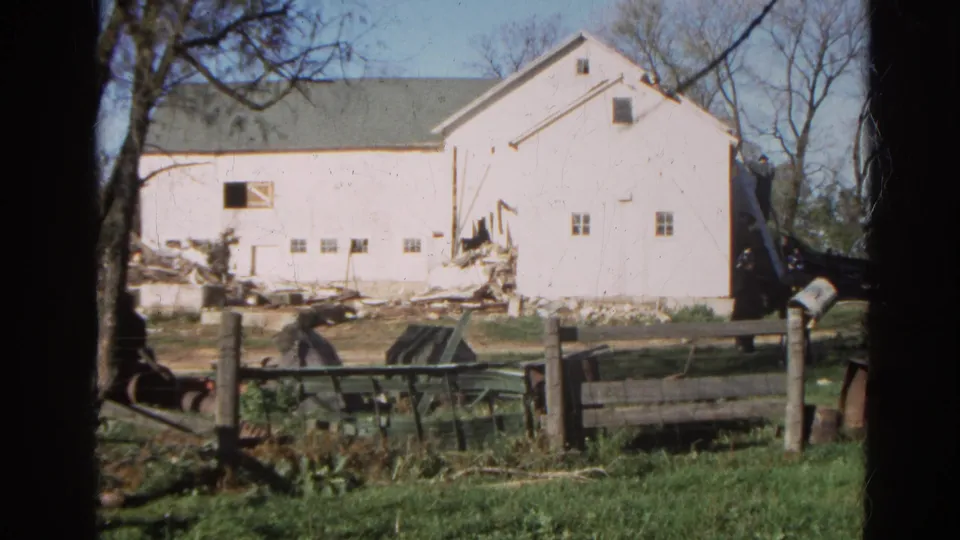 1968 Wauconda, Illinois frame with the white barn filling more of the view, showing damaged lower siding and debris near the foundation.