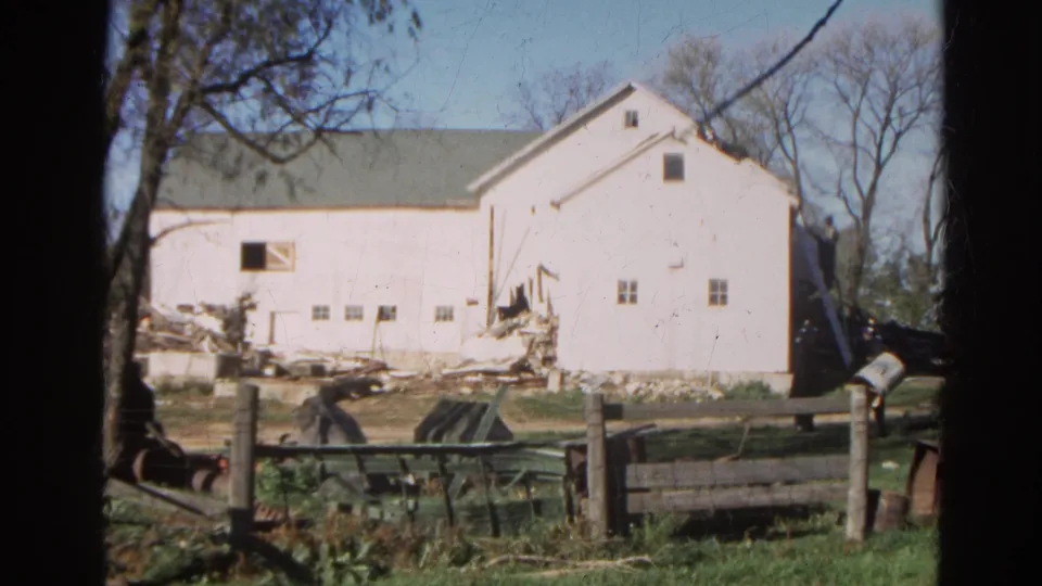 1968 Wauconda, Illinois 8mm frame showing a white rural barn with scattered demolition debris, fencing, and bare trees.