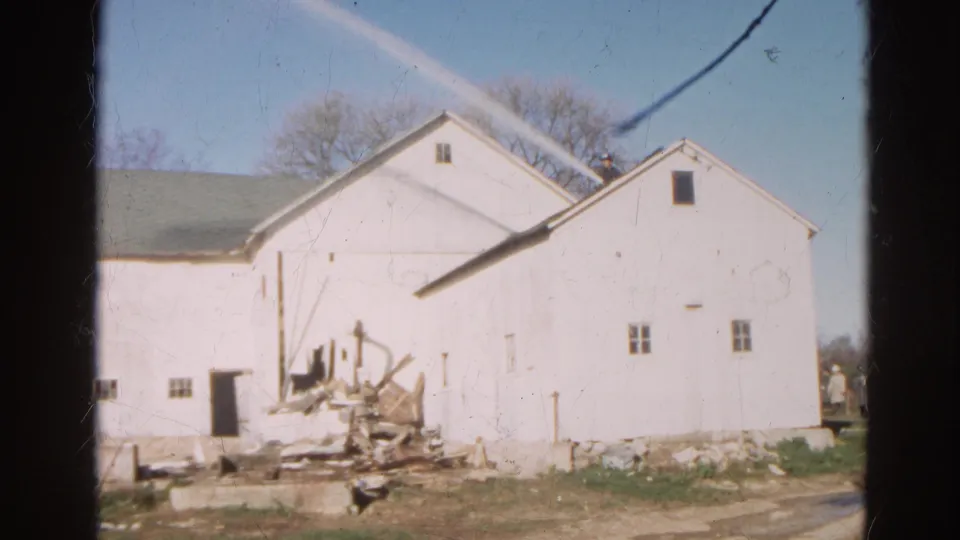 1968 Wauconda farm view of a white barn exterior with a debris pile and apparent structural damage near one side.