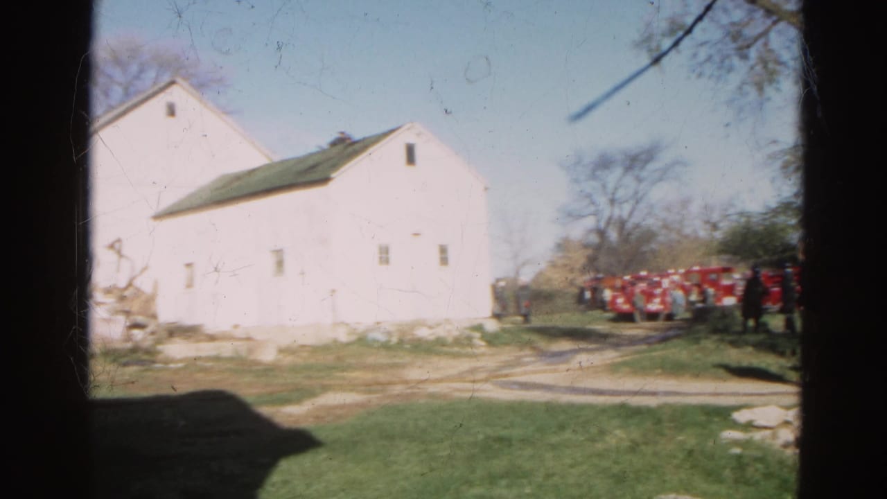 White farm building with red fire trucks parked nearby and dark film borders.
