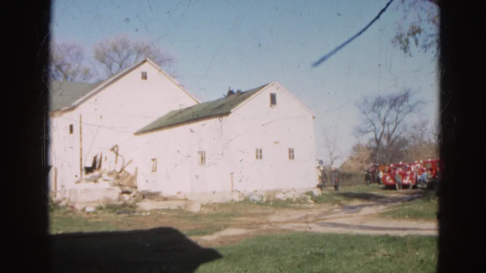 1968 Wauconda, Illinois frame showing a damaged white farm building, red fire trucks, and people standing nearby.