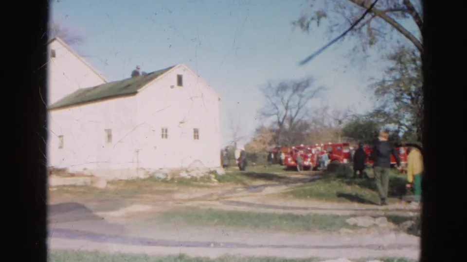 1968 Wauconda, Illinois frame showing people near a white rural building while red fire trucks line the driveway.