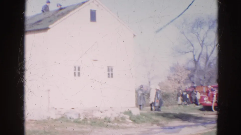 8mm frame of a large white building in Wauconda with firefighters and red trucks partly visible at the edge.
