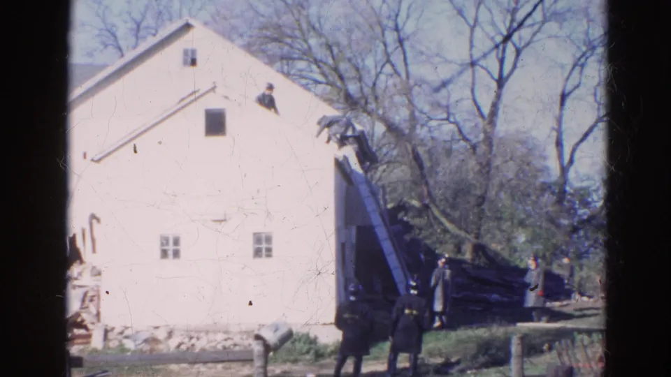 1968 Wauconda frame showing firefighters, an extended ladder and the side of a white building near bare trees.
