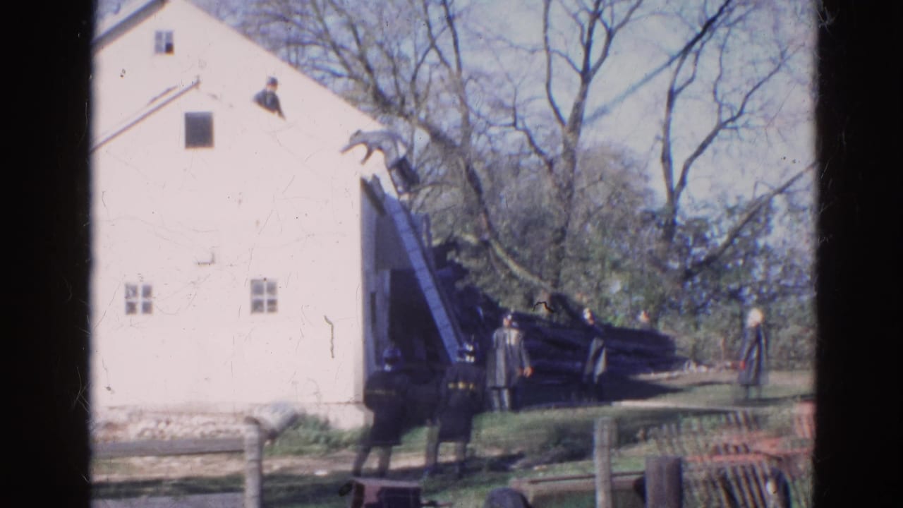 1968 Wauconda, Illinois 8mm frame showing a man at a roof ladder on a white house with uniformed adults observing below.