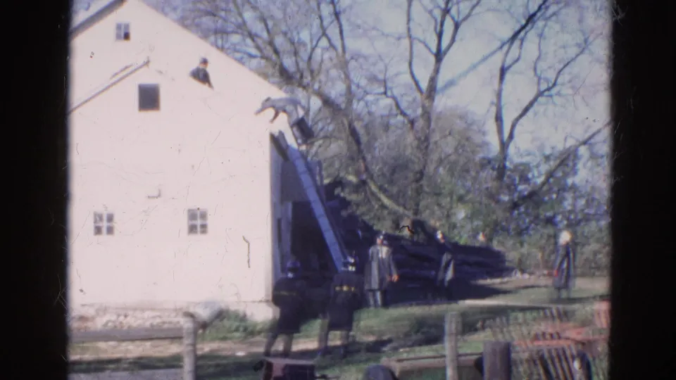 1968 Wauconda, Illinois 8mm frame showing a man at a roof ladder on a white house with uniformed adults observing below.