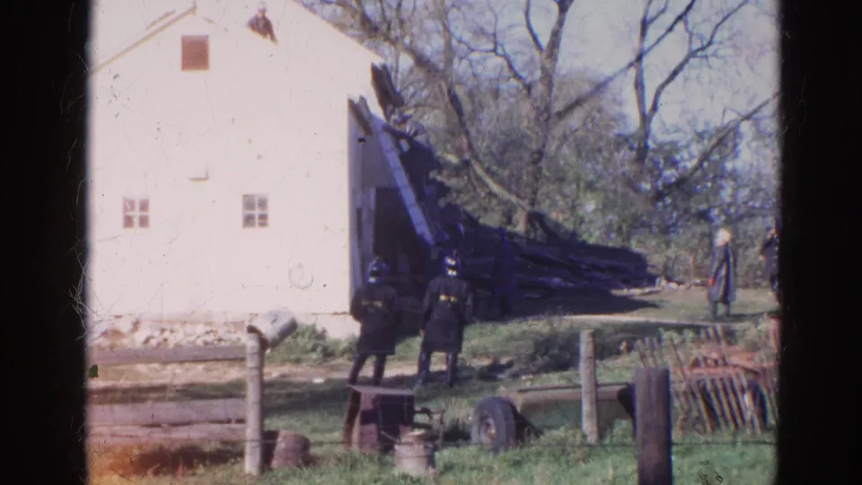 1968 Wauconda, Illinois frame showing a man descending a roof ladder beside a white house as uniformed adults observe.