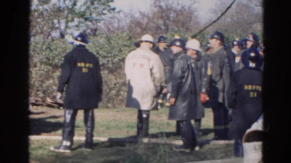 1968 Wauconda frame showing firefighters from behind, including a white coat with fire department lettering and dark coats with helmet or back markings.