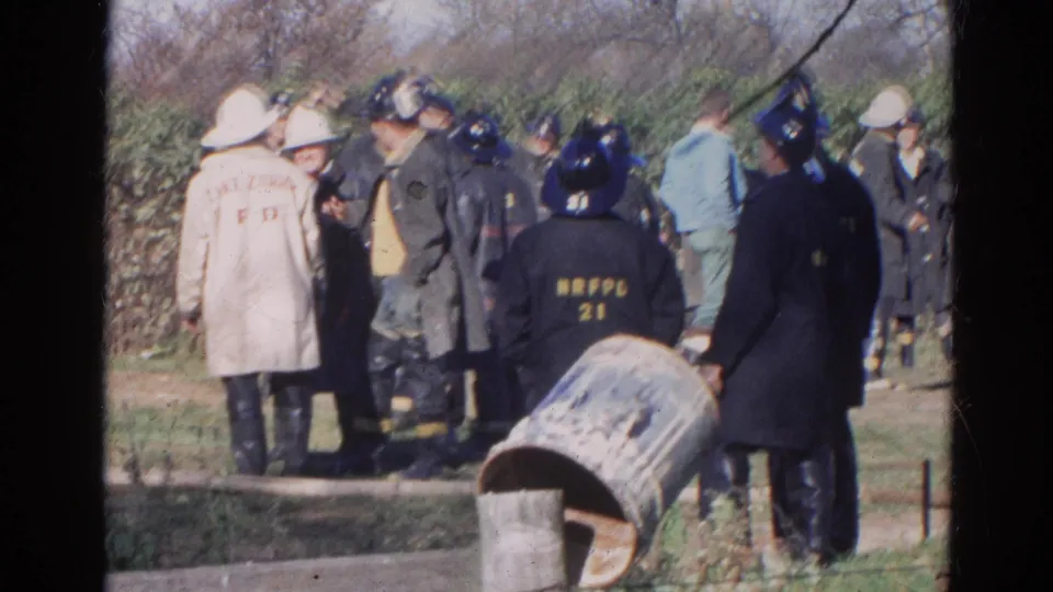 A home-movie view shows firefighters in 1968 Wauconda, including dark turnout gear, helmets, and a beige Lake Zurich F.D. coat.