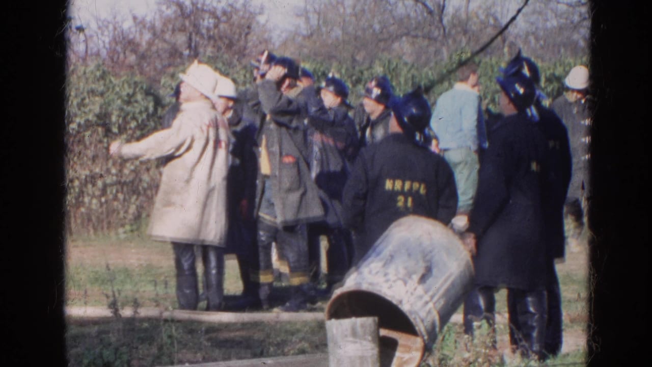 1968 Wauconda home-movie frame showing firefighters in helmets and raincoats gathered outdoors during an apparent response.