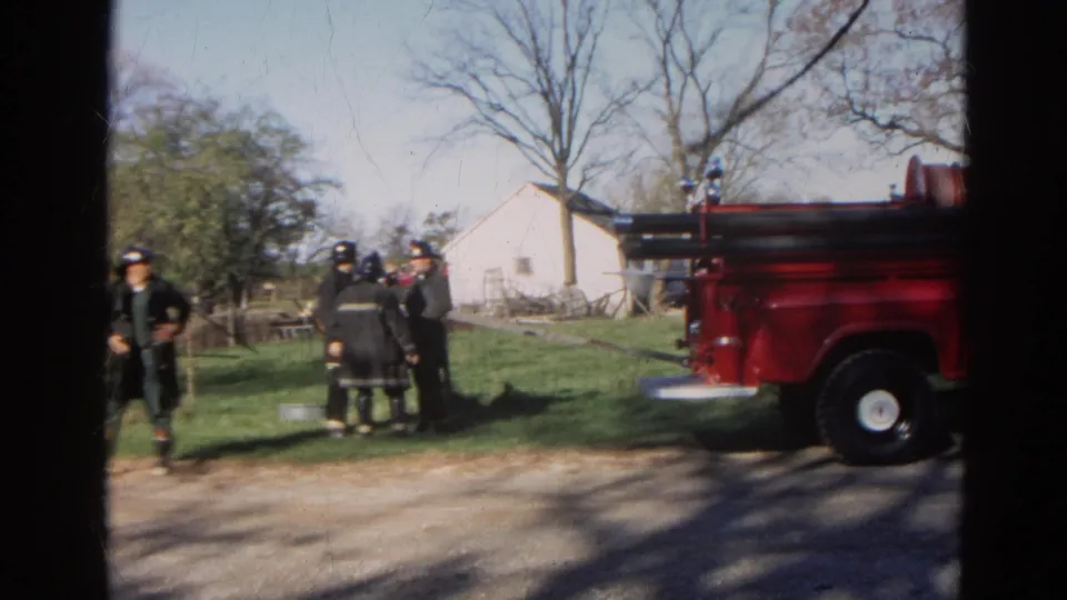 1968 Wauconda frame showing firefighters in grass with a red fire truck at right and white rural buildings behind them.