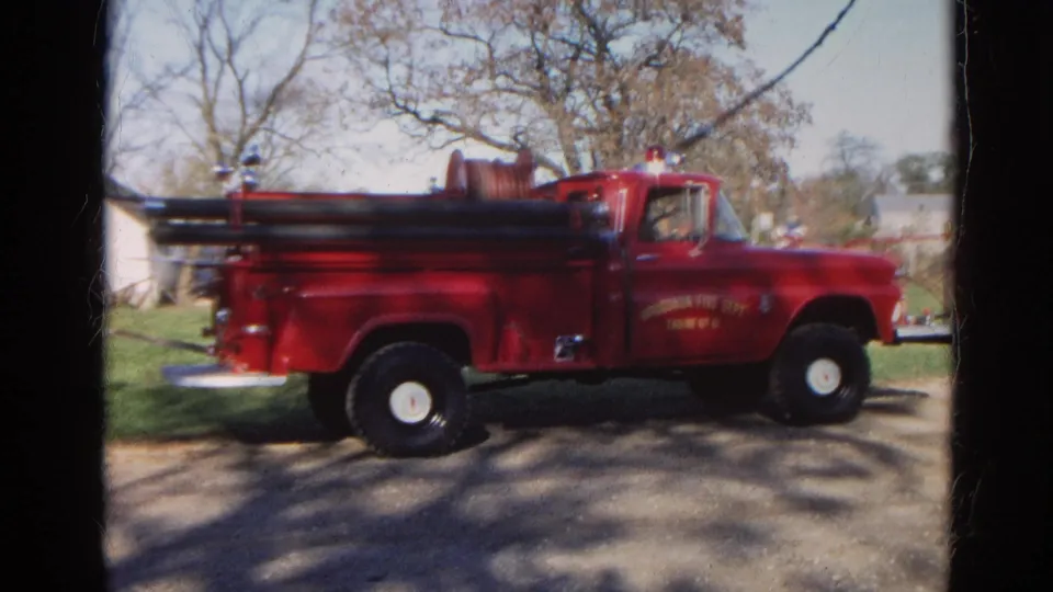 1968 Wauconda, Illinois frame with a red fire department truck seen broadside on a rural road, with trees and open ground behind it.