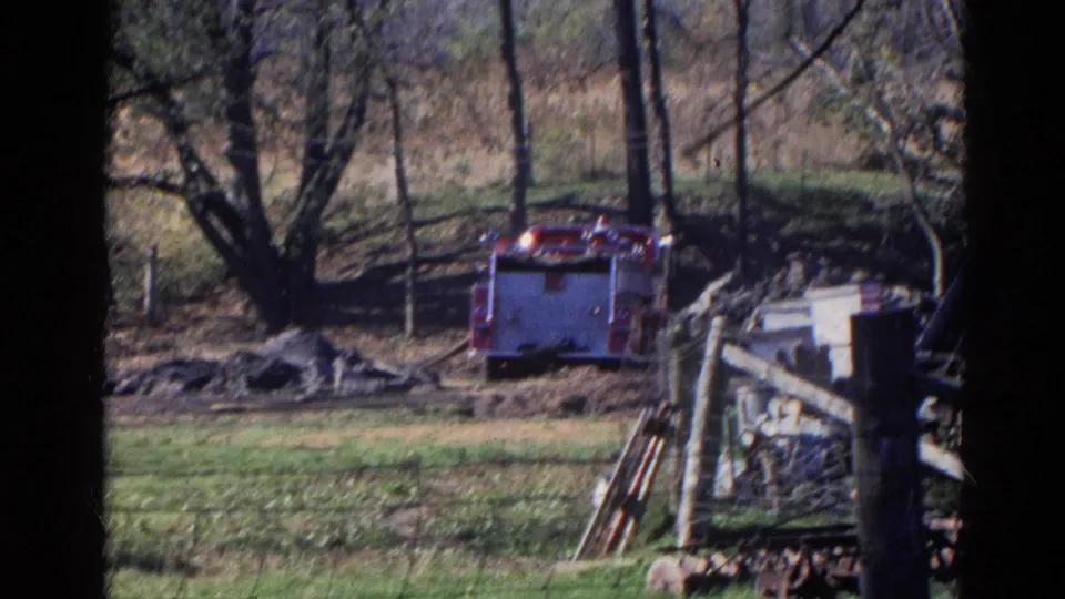 1968 Wauconda, Illinois frame showing the rear of a red fire truck in a field, with fencing, debris, trees, and yard equipment in view.