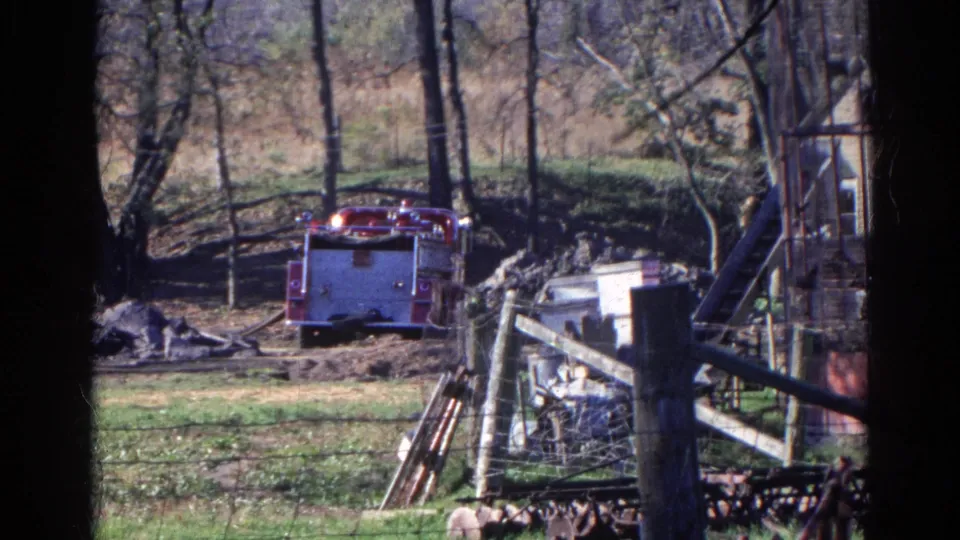 1968 Wauconda, Illinois frame showing a red fire truck positioned near trees, fencing, debris, and a yard structure in a rural setting.