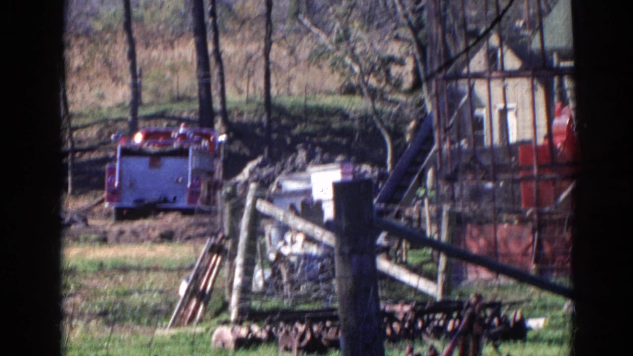 Red fire truck parked or moving beyond a wooden fence in a rural yard.