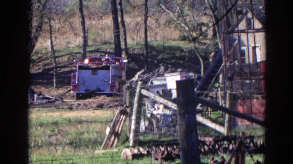 8mm home-movie frame of a red fire truck near fencing and debris in Wauconda, Illinois, with bare trees and a small structure behind it.