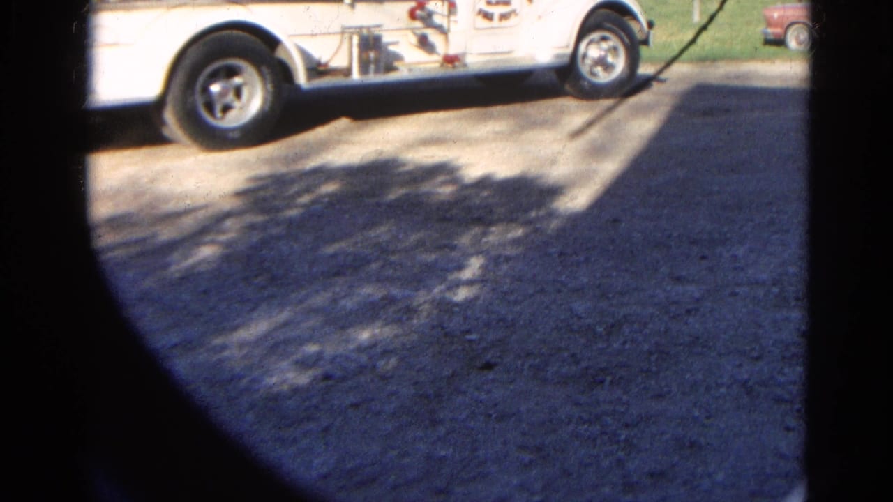 Partial white fire truck at the top of a circular 8mm frame with pavement and tree shadows below.