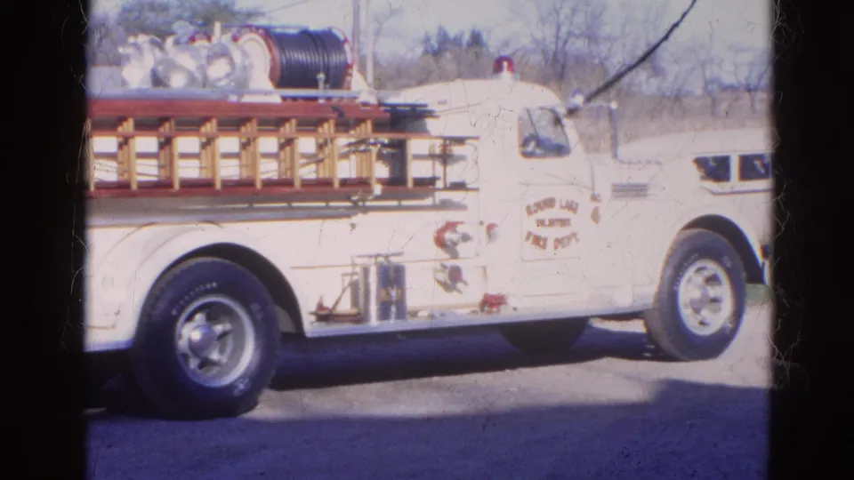 1968 Wauconda home-movie frame showing a white fire truck from the side with Round Lake Fire Department lettering partly visible.