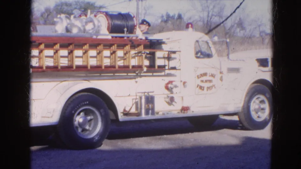 Broadside 1968 8mm view of a white fire truck in Wauconda, Illinois with equipment mounted along its side.