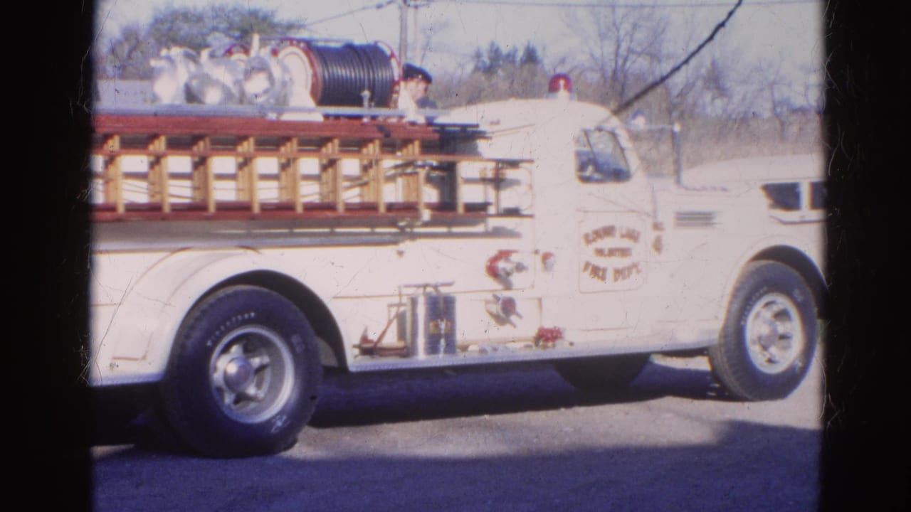 White volunteer fire department truck with ladder rack and hose reel parked outdoors.