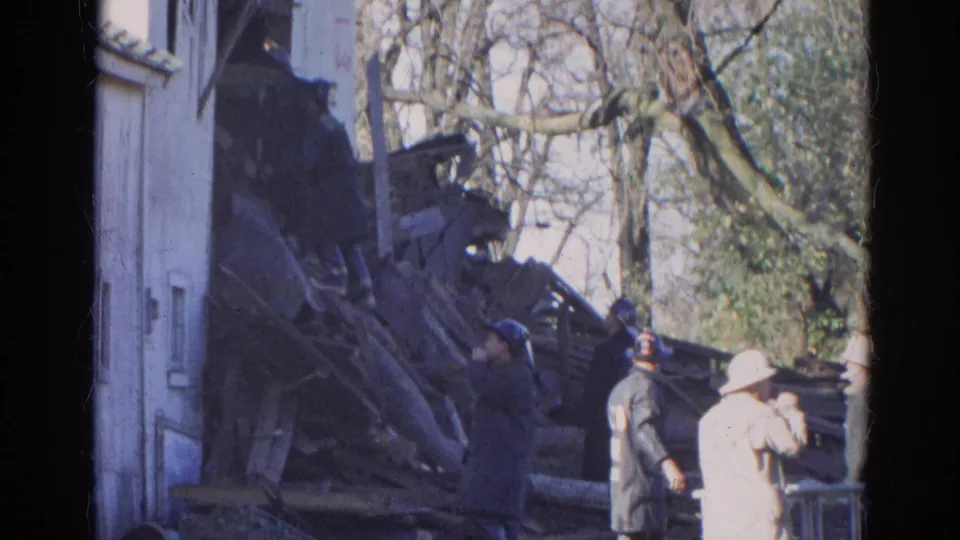 1968 Wauconda frame with firefighters and onlookers gathered near dark wreckage, bare branches, and the side of a white building.