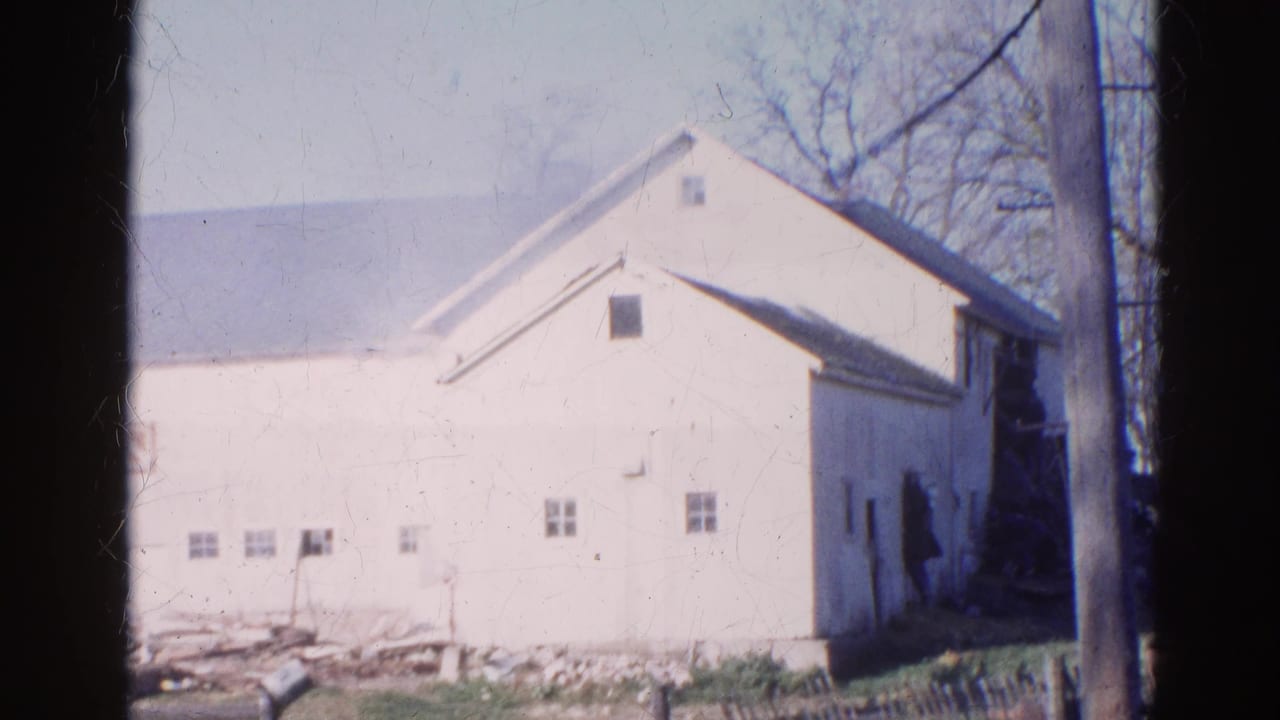 White farmhouse in sunlight with debris and fencing in the foreground.