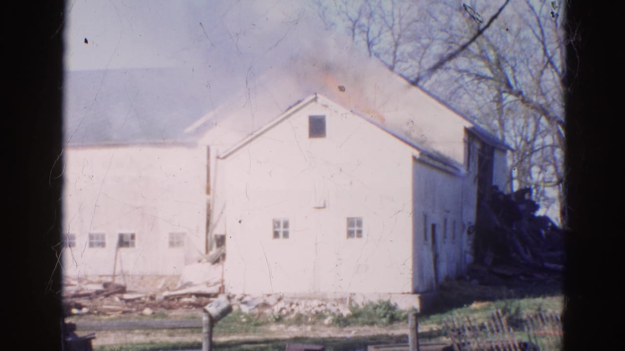 1968 Wauconda, Illinois 8mm frame of a white barn as smoke thickens near the roof and charred material appears beside the structure.