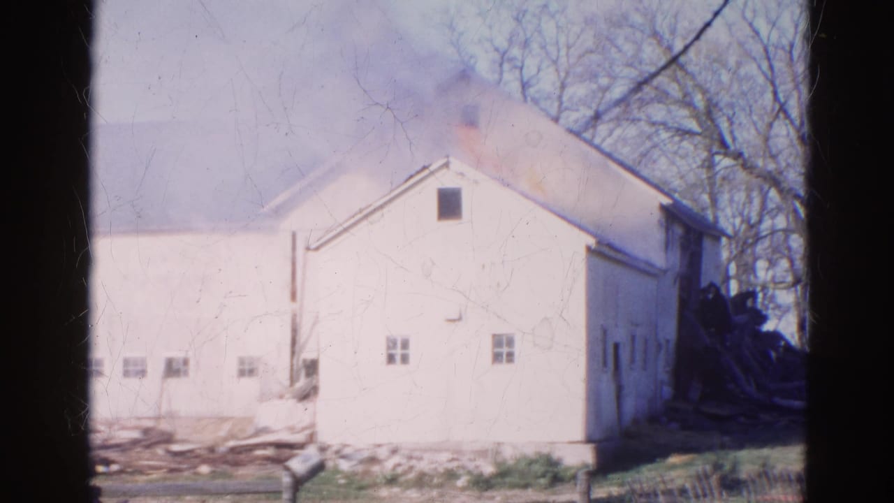 1968 Wauconda, Illinois 8mm frame showing heavier smoke over a white barn roof, with leafless trees and scattered material at ground level.