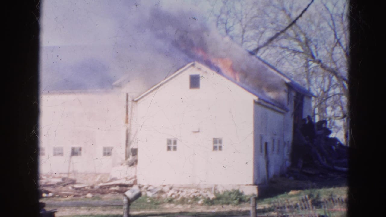 1968 Wauconda, Illinois 8mm frame showing a white barn burning, with flames along the roofline and smoke rising behind leafless trees.