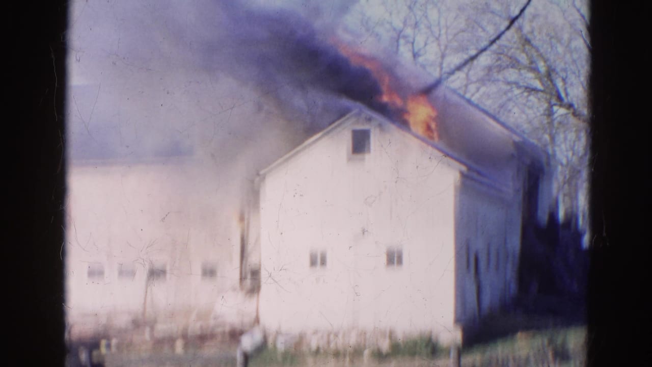 White barn roof burning with smoke spreading across the upper frame.