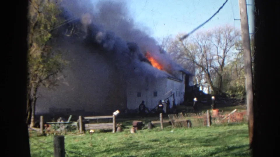 1968 8mm frame from Wauconda showing dense smoke over a rural outbuilding fire with firefighters visible near the structure.